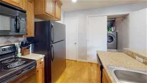 Kitchen with light hardwood / wood-style flooring, black appliances, tasteful backsplash, sink, and washer / clothes dryer