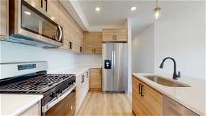 Kitchen with light hardwood / wood-style flooring, light brown cabinets, sink, pendant lighting, and appliances with stainless steel finishes