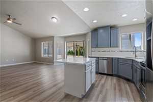Kitchen with ceiling fan, a kitchen island, sink, stainless steel dishwasher, and light hardwood / wood-style flooring