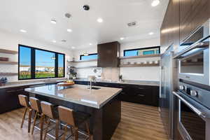 Kitchen featuring a kitchen island with sink, a breakfast bar, light stone countertops, light hardwood / wood-style flooring, and tasteful backsplash