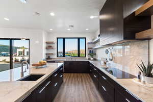 Kitchen featuring light stone counters, sink, wall chimney range hood, black electric cooktop, and dark hardwood / wood-style flooring