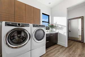 Laundry area with wood-type flooring, cabinets, sink, and separate washer and dryer