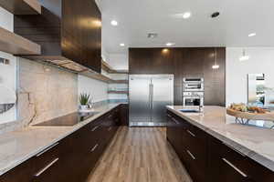 Kitchen with backsplash, light hardwood / wood-style floors, stainless steel appliances, and light stone counters