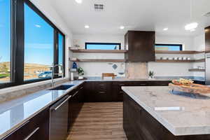 Kitchen with dark brown cabinetry, wall chimney exhaust hood, sink, stainless steel dishwasher, and hardwood / wood-style flooring