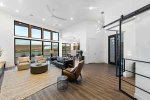 Living room with ceiling fan, a towering ceiling, a barn door, and dark hardwood / wood-style floors