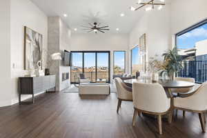 Dining area featuring ceiling fan with notable chandelier, a healthy amount of sunlight, a towering ceiling, and dark hardwood / wood-style floors