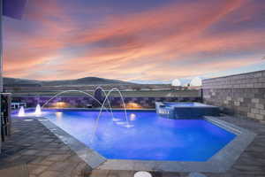 Pool at dusk featuring a mountain view, pool water feature, and an in ground hot tub