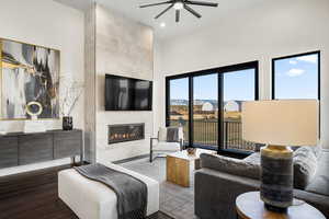 Living room featuring dark wood-type flooring, ceiling fan, and a fireplace