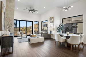 Living room featuring a high ceiling, ceiling fan with notable chandelier, and dark wood-type flooring