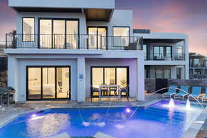 Back house at dusk featuring a patio, a balcony, and pool water feature