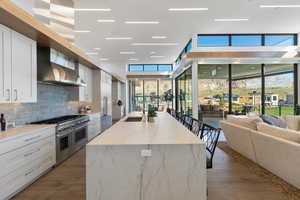 Kitchen with wall chimney exhaust hood, sink, tasteful backsplash, white cabinetry, and range with two ovens