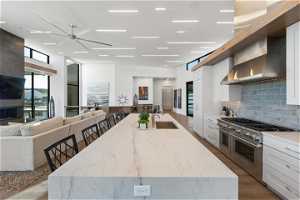 Kitchen with double oven range, a center island with sink, and wall chimney exhaust hood