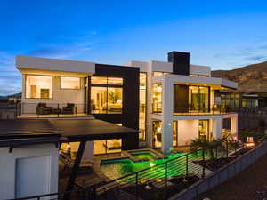 Back house at dusk featuring a balcony, a patio, and a pool with hot tub