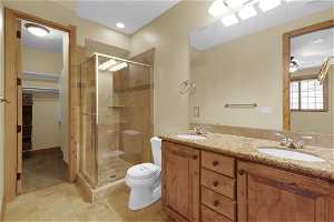 On-suite bathroom with walk-in shower, walk-in closet, double vanity, toilet, tile floors, and ceiling fan