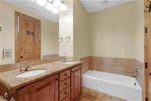 Bathroom with large vanity, dual sinks, a bath to relax in, and tile flooring