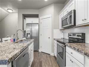 Kitchen featuring dark wood-type flooring, stainless steel appliances, white cabinetry, tasteful backsplash, and sink