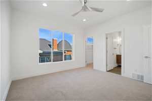 Unfurnished bedroom featuring a walk in closet, ensuite bathroom, ceiling fan, and light carpet