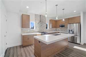 Kitchen featuring wall chimney exhaust hood, appliances with stainless steel finishes, tasteful backsplash, and sink