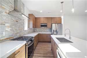 Kitchen with dark wood-type flooring, tasteful backsplash, sink, stainless steel appliances, and wall chimney range hood