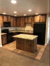 Kitchen with light stone counters, light tile flooring, sink, black appliances, and a center island
