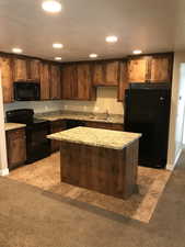 Kitchen with light stone counters, light tile flooring, sink, black appliances, and a center island