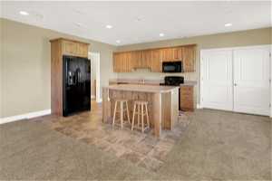 Basement Kitchen featuring a center island with sink, black appliances, a kitchen breakfast bar, sink, and light colored carpet