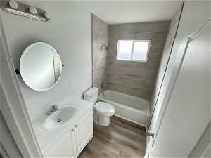 Full bathroom with LVP wood-style flooring, vanity, tiled shower / bath combo, and toilet