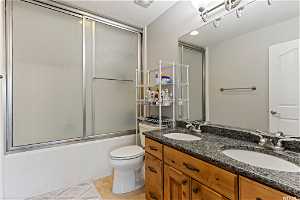 Full bathroom featuring shower / bath combination with glass door, toilet, tile flooring, large vanity, and double sink