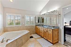 Bathroom featuring vaulted ceiling, tile flooring, tiled tub, and double vanity