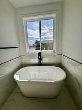 Bathroom with tile walls, a bathtub, and tile patterned floors