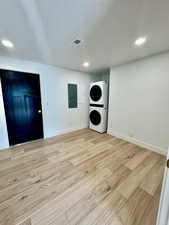 Laundry area featuring electric panel, light hardwood / wood-style flooring, and stacked washer / dryer