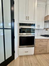 Kitchen with double oven, light wood-type flooring, white cabinetry, and tasteful backsplash