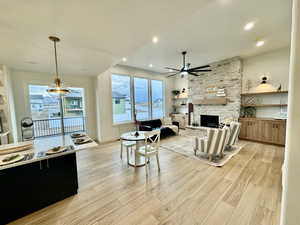 Living room with light wood-type flooring, a stone fireplace, and ceiling fan