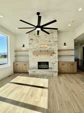 Unfurnished living room featuring light wood-type flooring, a stone fireplace, and ceiling fan