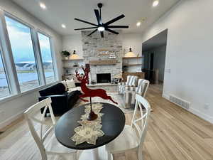 Living room featuring ceiling fan, a stone fireplace, and light hardwood / wood-style flooring