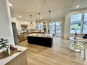 Kitchen featuring a large island, hanging light fixtures, light hardwood / wood-style flooring, white cabinets, and appliances with stainless steel finishes