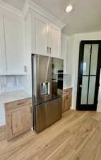 Kitchen with light wood-type flooring, stainless steel refrigerator with ice dispenser, white cabinetry, and backsplash