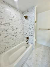 Bathroom with a textured ceiling, tiled shower / bath combo, and toilet