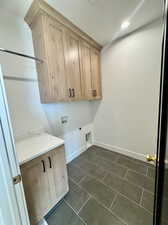 Washroom featuring hookup for a washing machine, hookup for an electric dryer, dark tile patterned floors, and cabinets