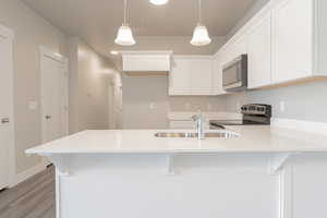 Kitchen with pendant lighting, appliances with stainless steel finishes, light wood-type flooring, sink, and white cabinetry