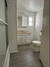 Full bathroom with combined bath / shower with glass door, vanity, a textured ceiling, toilet, and wood-type flooring