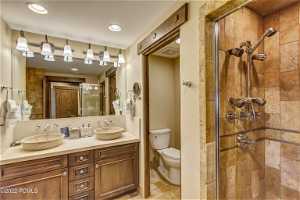 Bathroom with oversized vanity, walk in shower, double sink, toilet, and tile flooring