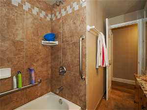 Bathroom with vanity, tiled shower / bath combo, a textured ceiling, and wood-type flooring