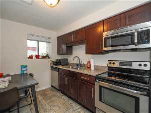 Kitchen featuring dark brown cabinets, stainless steel appliances, light stone counters, sink, and light tile floors