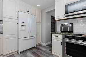 Kitchen featuring tasteful backsplash, white cabinetry, dark wood-type flooring, and stainless steel appliances