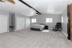 Carpeted bedroom featuring lofted ceiling with beams, ceiling fan, a textured ceiling, and two closets