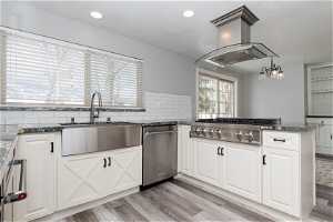 Kitchen with tasteful backsplash, island range hood, white cabinets, and light wood-type flooring