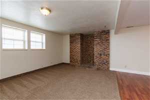 Unfurnished living room featuring a textured ceiling, dark carpet, and a brick fireplace