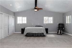 Carpeted bedroom with ceiling fan, a textured ceiling, and vaulted ceiling