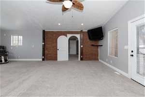 Unfurnished living room with brick wall, ceiling fan, a textured ceiling, and light carpet